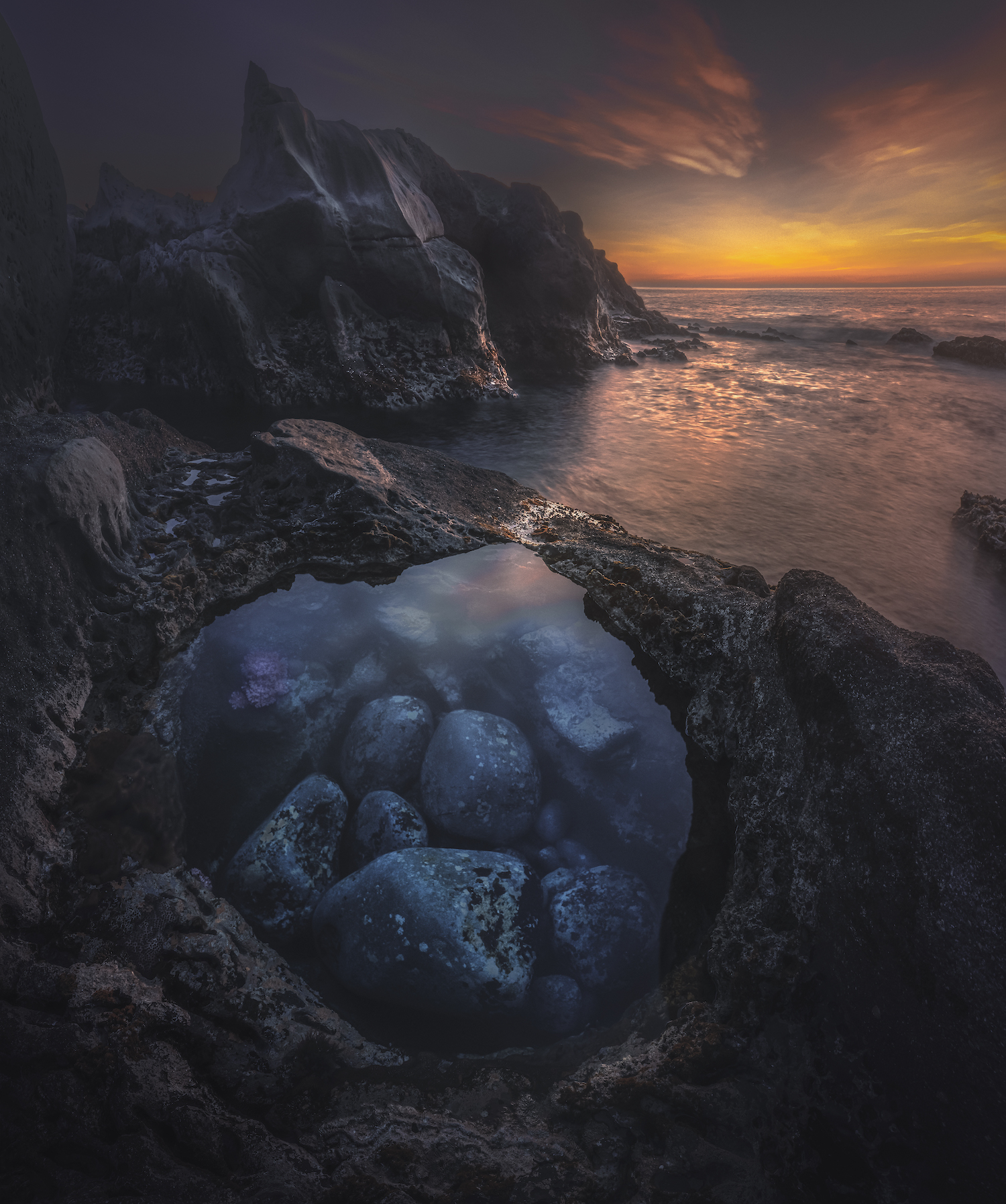 rocks in a small pool of water in the foreground. sunset in the background next to imposing jutting peaks